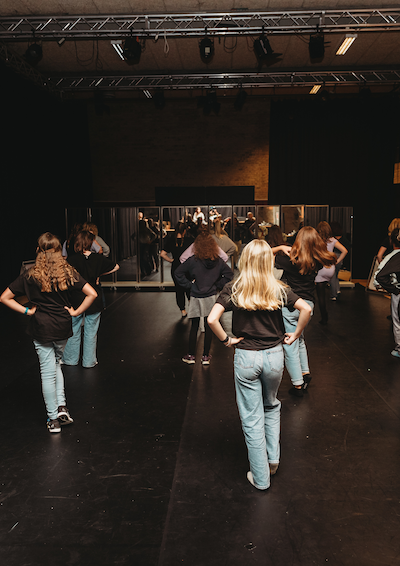 Foto af piger som står med ryggen til mod et spejl og danser